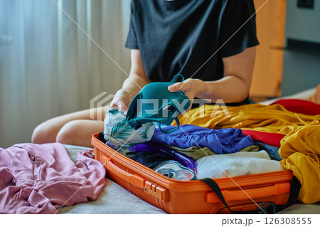 Woman packing colorful clothes into orange suitcase for vacation Woman packing colorful clothes into orange suitcase for vacation 126308555