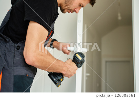 Man installs door in apartment during renovation, using cordless screwdriver 126308561