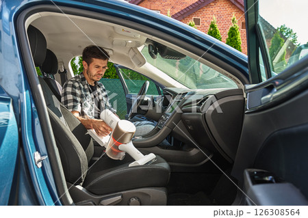 Man cleaning car dashboard with handheld vacuum cleaner 126308564