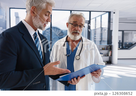 Doctor talking with hospital manager, walking down hospital hallway. Doctor talking with hospital manager, walking down hospital hallway. 126308652