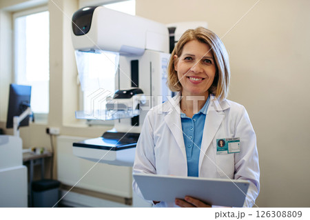 Smiling doctor standing next to mammogram machine in hospital Smiling doctor standing next to mammogram machine in hospital 126308809