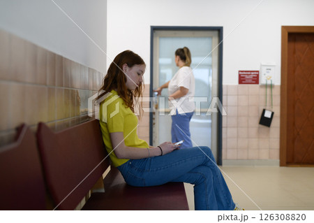 Teenage girl waiting alone in hospital waiting area, scrolling on phone. Teenage girl waiting alone in hospital waiting area, scrolling on phone. 126308820