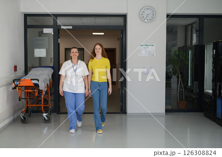 Nurse walking with teenage patient in hospital waiting room. 126308824