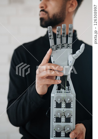 Portrait of young engineer holding robotic arm. 126308997