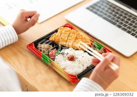 会社のデスクでトンカツ弁当を食べるミドル女性 126309332