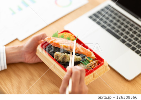 会社のデスクでシャケ弁当を食べるミドル女性 126309366