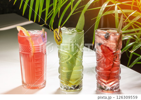 Colorful tropical cocktails with ice and fresh fruit garnishes on a sunlit table. lemonade, cold summer drink 126309559