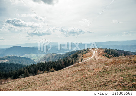 Winding mountain road stretching through scenic hills under a cloudy sky 126309563