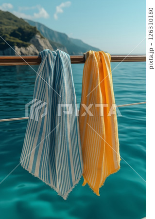Two striped towels, one blue and one yellow, hang over a railing against the backdrop of the open sea. Two striped towels, one blue and one yellow, hang over a railing against the backdrop of the open sea. 126310180