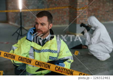Man is talking by phone. Detectives are collecting evidence in a crime scene near dead body 126312461