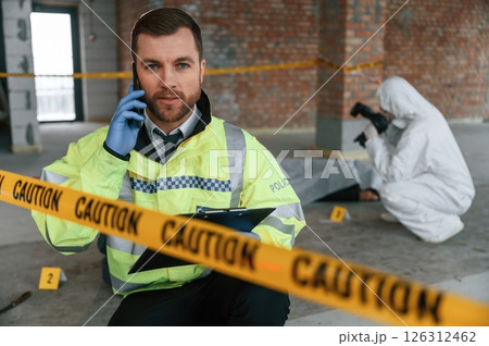 Man is talking by phone. Detectives are collecting evidence in a crime scene near dead body 126312462