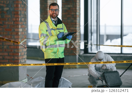 Man is standing and smiling. Detectives are collecting evidence in a crime scene near dead body 126312471