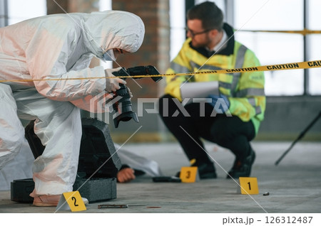 Woman is using camera, making photos. Detectives are collecting evidence in a crime scene near dead body Woman is using camera, making photos. Detectives are collecting evidence in a crime scene near dead body 126312487