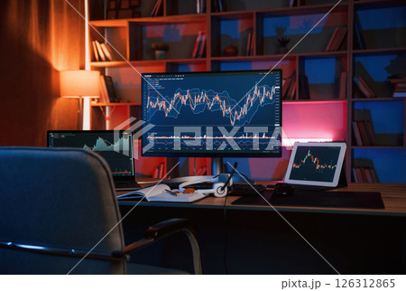 Computer with stock exchange graph on display is in the dark room with neon lighting Computer with stock exchange graph on display is in the dark room with neon lighting 126312865