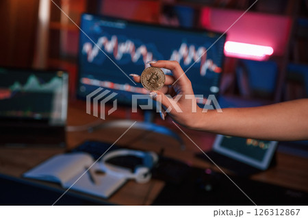 Close up view of woman's hand that holding bitcoin against computer display and tablet with graphs Close up view of woman's hand that holding bitcoin against computer display and tablet with graphs 126312867