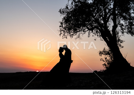 Silhouette of a couple standing next to a tree at sunset Silhouette of a couple standing next to a tree at sunset 126313194