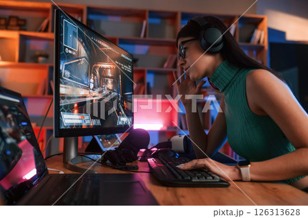 Side view. Young pretty female gamer is playing shooter. Neon lighting Side view. Young pretty female gamer is playing shooter. Neon lighting 126313628
