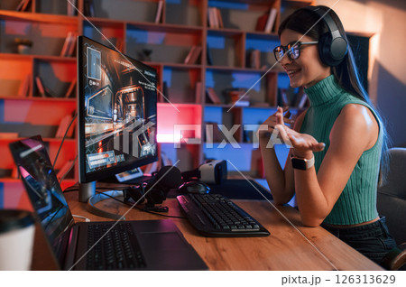 Side view. Young pretty female gamer is playing shooter. Neon lighting Side view. Young pretty female gamer is playing shooter. Neon lighting 126313629