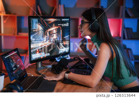 In glasses. Young pretty female gamer is playing shooter. Neon lighting In glasses. Young pretty female gamer is playing shooter. Neon lighting 126313644