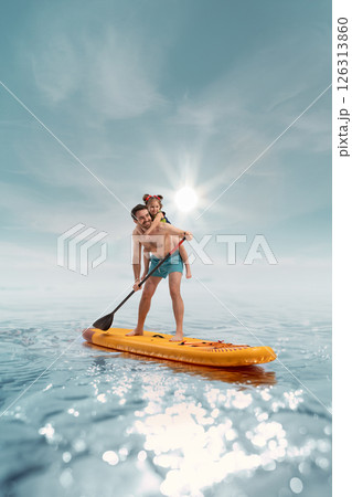 Happy smiling father standing on paddle board with his little happy child, daughter sitting on his back against sunny sea background 126313860