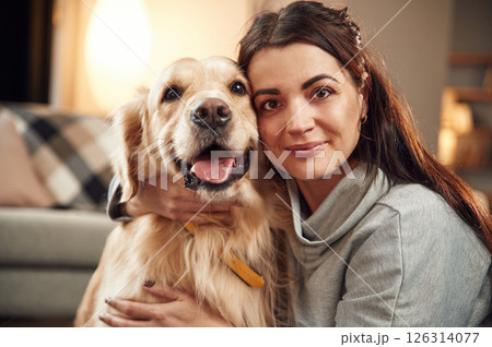 Looking at the camera. Woman is with golden retriever dog at home 126314077