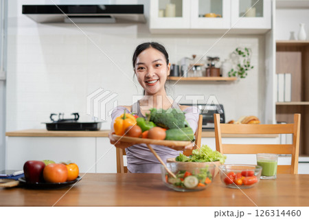 Fit woman enjoys healthy fresh vegetables and fruits breakfast sitting in the kitchen. Fit woman enjoys healthy fresh vegetables and fruits breakfast sitting in the kitchen. 126314460