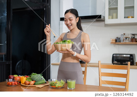 Fit woman enjoys healthy fresh vegetables and fruits breakfast sitting in the kitchen. Fit woman enjoys healthy fresh vegetables and fruits breakfast sitting in the kitchen. 126314492