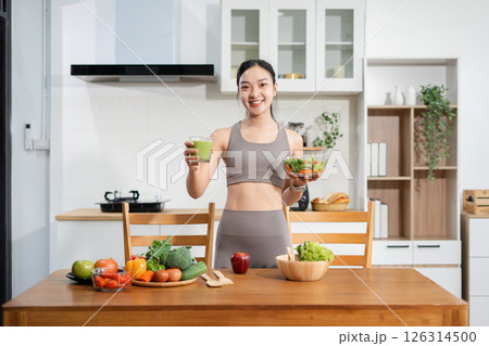 Fit woman enjoys healthy fresh vegetables and fruits breakfast sitting in the kitchen. Fit woman enjoys healthy fresh vegetables and fruits breakfast sitting in the kitchen. 126314500