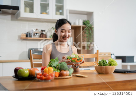 Fit woman enjoys healthy fresh vegetables and fruits breakfast sitting in the kitchen. Fit woman enjoys healthy fresh vegetables and fruits breakfast sitting in the kitchen. 126314503