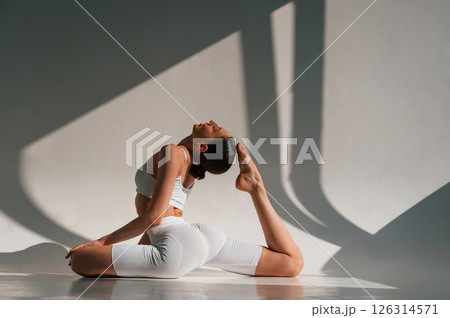 Yoga exercises on the floor. Beautiful sunlight. Young caucasian woman with slim body shape is indoors in the studio Yoga exercises on the floor. Beautiful sunlight. Young caucasian woman with slim body shape is indoors in the studio 126314571