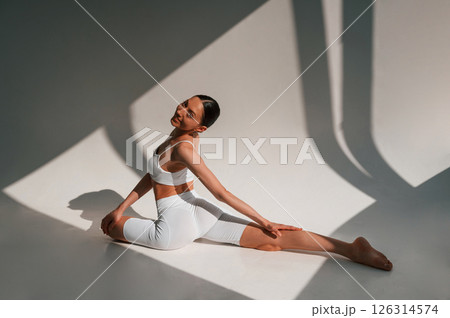 Yoga exercises on the floor. Beautiful sunlight. Young caucasian woman with slim body shape is indoors in the studio Yoga exercises on the floor. Beautiful sunlight. Young caucasian woman with slim body shape is indoors in the studio 126314574