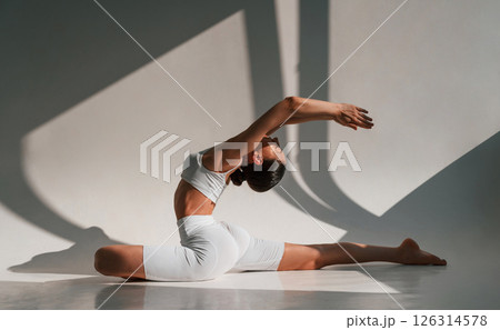 Doing stretching on the floor. Young caucasian woman with slim body shape is indoors in the studio Doing stretching on the floor. Young caucasian woman with slim body shape is indoors in the studio 126314578
