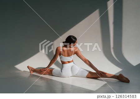 Doing stretching on the floor. Young caucasian woman with slim body shape is indoors in the studio 126314583