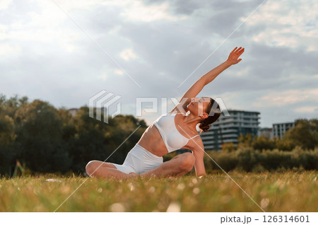 Doing stretching yoga exercises. Young caucasian woman with slim body shape is in the fitness clothes outdoors 126314601