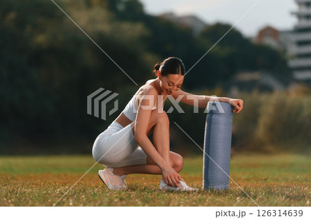 Sitting with yoga mat. Young caucasian woman with slim body shape is in the fitness clothes outdoors 126314639
