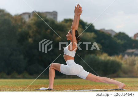 Warrior asana. Young caucasian woman with slim body shape is in the fitness clothes outdoors 126314647