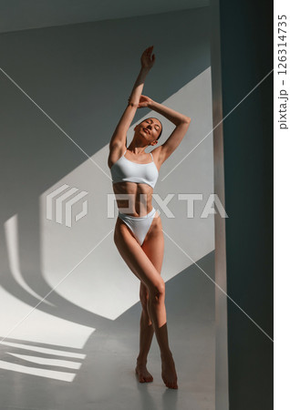 Illuminated by sunlight. Young caucasian woman with slim body shape is indoors in the studio Illuminated by sunlight. Young caucasian woman with slim body shape is indoors in the studio 126314735