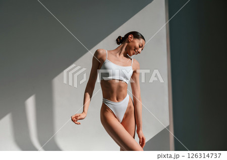 Illuminated by sunlight. Young caucasian woman with slim body shape is indoors in the studio Illuminated by sunlight. Young caucasian woman with slim body shape is indoors in the studio 126314737
