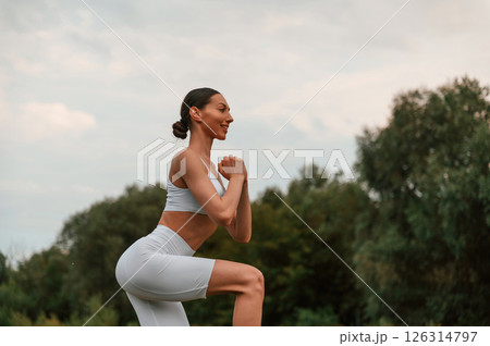 Doing squats. Young caucasian woman with slim body shape is in the fitness clothes outdoors 126314797