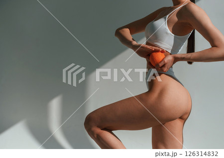 Fresh orange in hands. Young caucasian woman with slim body shape is indoors in the studio 126314832