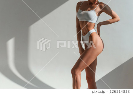 Indoors against the wall, beautiful sunlight. Young caucasian woman with slim body shape is indoors in the studio Indoors against the wall, beautiful sunlight. Young caucasian woman with slim body shape is indoors in the studio 126314838