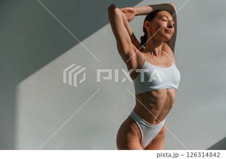 Indoors against the wall, beautiful sunlight. Young caucasian woman with slim body shape is indoors in the studio 126314842