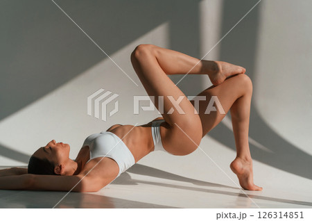 Peaceful mood. Lying down on the floor. Young caucasian woman with slim body shape is indoors in the studio Peaceful mood. Lying down on the floor. Young caucasian woman with slim body shape is indoors in the studio 126314851