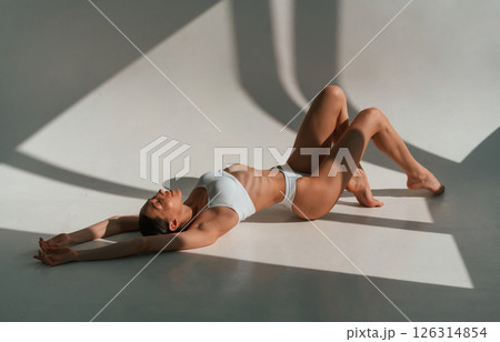 Peaceful mood. Lying down on the floor. Young caucasian woman with slim body shape is indoors in the studio Peaceful mood. Lying down on the floor. Young caucasian woman with slim body shape is indoors in the studio 126314854