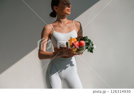 Holding vegetables and fruits. Young caucasian woman with slim body shape is indoors in the studio Holding vegetables and fruits. Young caucasian woman with slim body shape is indoors in the studio 126314930