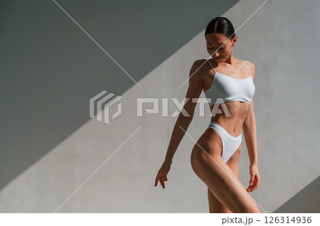 Standing against the wall and showing body. Young caucasian woman is indoors in the studio 126314936
