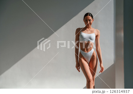 Standing against the wall and showing body. Young caucasian woman is indoors in the studio 126314937