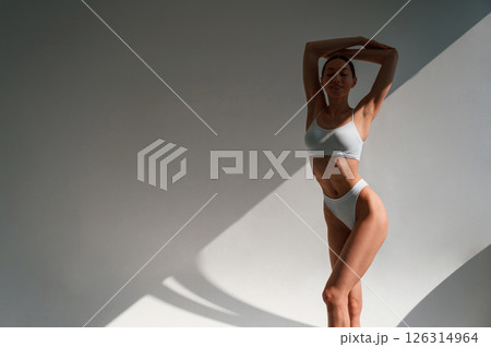 Against wall. Young caucasian woman with slim body shape is indoors in the studio Against wall. Young caucasian woman with slim body shape is indoors in the studio 126314964