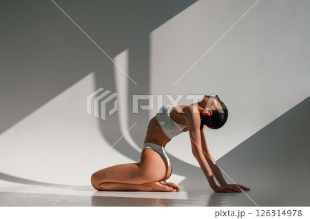 Exercise for the spine. Young caucasian woman with slim body shape is indoors in the studio Exercise for the spine. Young caucasian woman with slim body shape is indoors in the studio 126314978