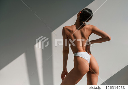 Rear view. Young caucasian woman with slim body shape is indoors in the studio Rear view. Young caucasian woman with slim body shape is indoors in the studio 126314988